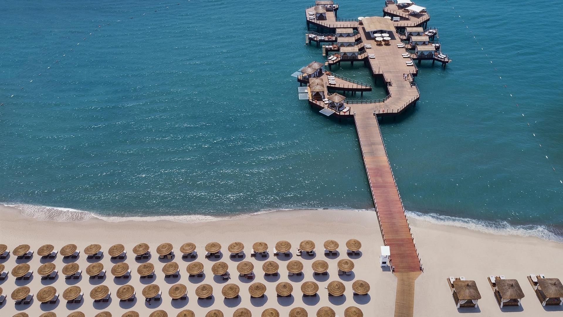 Aerial view of the sun loungers arranged by the sea and the wooden bridge deck near Titanic Mardan Palace