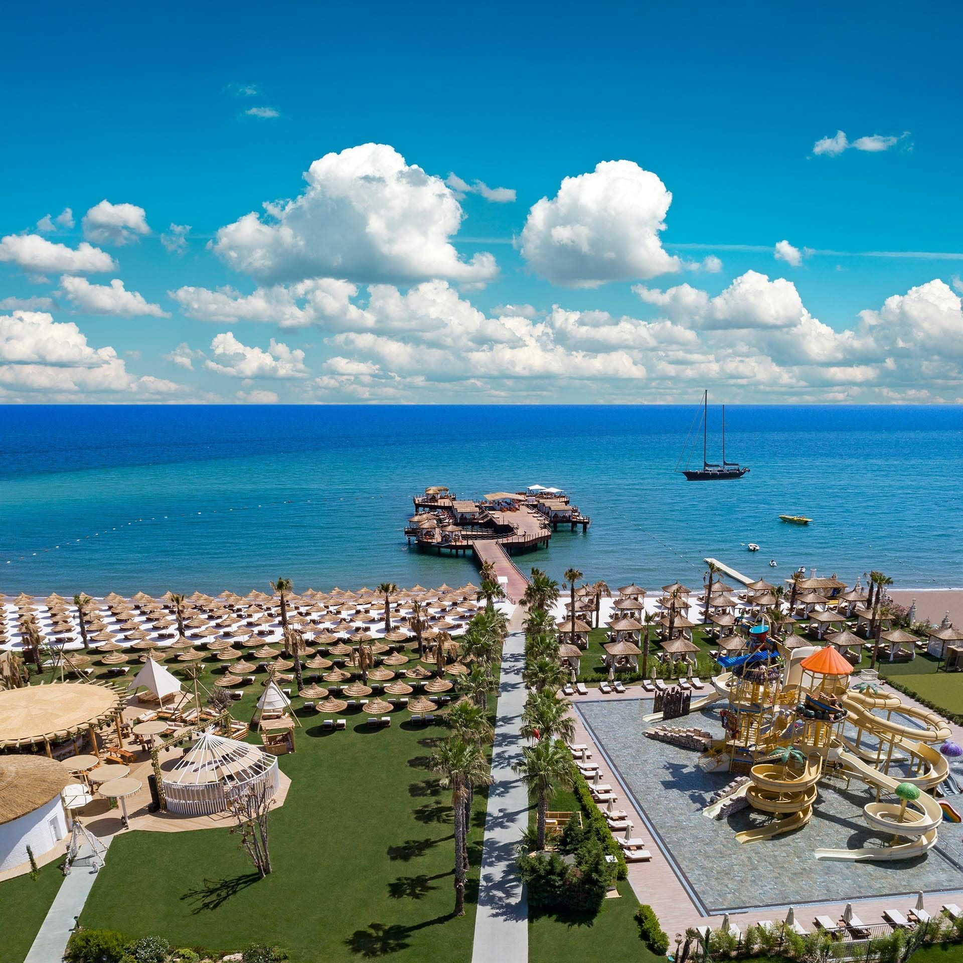 Overview beachfront resort with umbrellas, a pier, and a sailboat at Titanic Mardan Palace