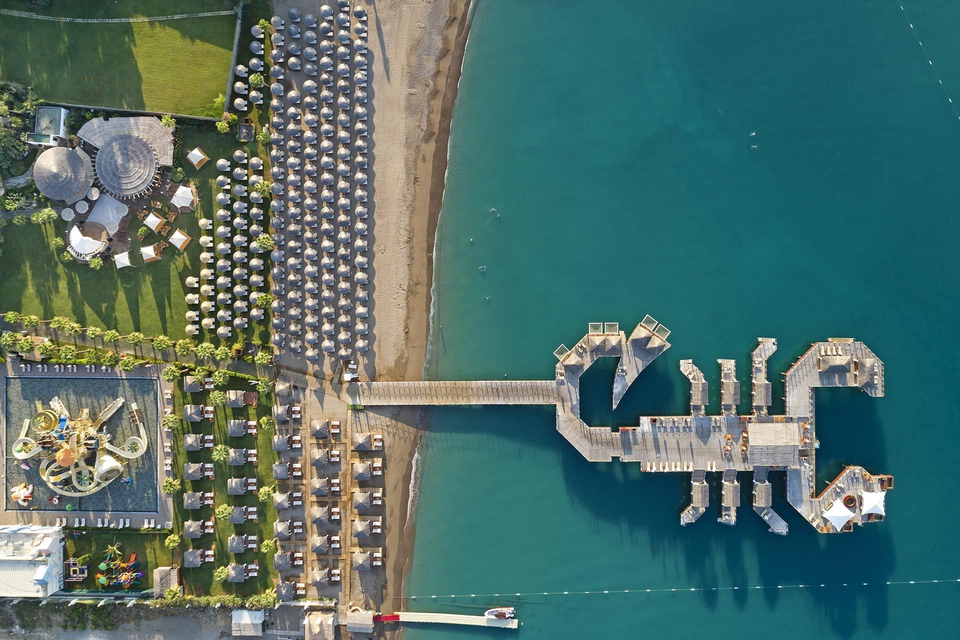 Overview beachfront resort with umbrellas, a pier, and a sailboat at Titanic Mardan Palace