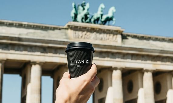 Hand holding a coffee cup with the Brandenburg Gate backdrop at Titanic Deluxe Golf Belek