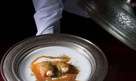 Chef presenting a plated dish with sauce and garnishes in a restaurant at Titanic Hotels